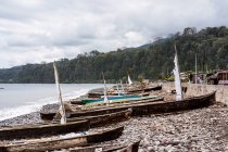 Old wooden boats moored on rocky coast near calm ocean against green trees in So Tom and Prncipe under cloudy sky in daylight — Stock Photo