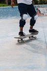 Anonymous young ethnic person in casual outfit wearing protective knee pads riding in skateboard in the skate park — Stock Photo
