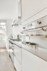 Interior de cozinha espaçosa com mobiliário branco minimalista e aparelhos contemporâneos em apartamento leve — Fotografia de Stock