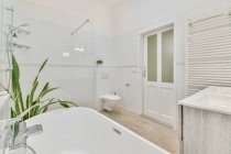 Modern minimalist styled bathroom interior with shower cabin and white ceramic bathtub near sink and mirror — Stock Photo
