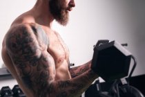 Side view of crop unrecognizable bodybuilder with tattoos standing with heavy dumbbells during workout in gym — Stock Photo