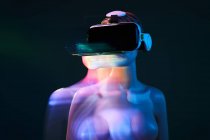 Maniquí de mujer en gafas VR futuristas colocadas bajo proyección brillante en habitación tenue - foto de stock