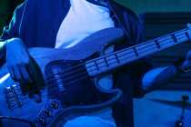 Crop анонімний чоловічий гітарист, який грає на електрогітарі в клубі з неоновим синім світлом — стокове фото