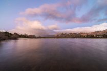 Acqua di mare che scorre contro la riva con ruvida montagna rocciosa contro il colorato cielo blu con nuvole bianche in natura al tramonto — Foto stock