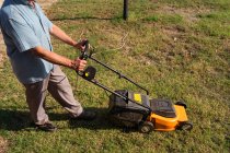 From above side view of male gardener mowing grassy lawn near bushes and trees in summer — Stock Photo