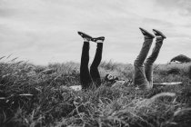 Черно-белый вид сбоку веселых друзей в повседневной одежде лежащих с поднятыми ногами на травянистом поле в природе при дневном свете — стоковое фото