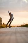 Ground level of full body of male in casual wear performing stunt on longboard on paved walkway — Stock Photo