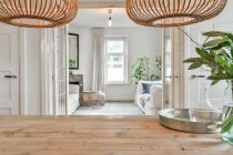 Mesa de madeira com ramos de plantas em vaso sob lâmpadas penduradas contra a sala de estar com janela em casa — Fotografia de Stock