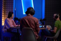 Konzentrierte junge Kolleginnen und Kollegen in Freizeitkleidung und Kopfhörern sitzen mit Mikrofonen am Tisch und kommunizieren während der Aufzeichnung eines Podcasts im modernen Studio — Stockfoto