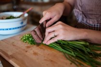 Von oben bis zur Unkenntlichkeit zerkleinert eine Frau frische grüne Kräuter auf einem Holzschneidebrett, während sie in der Küche das Abendessen zubereitet — Stockfoto