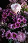 Аромат свежих красочных пионов и хризантем в стеклянной вазе на деревянном столе в темной комнате — стоковое фото