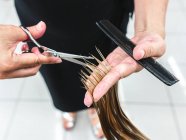 Crop unrecognizable hairdresser using scissors to cut fair hair of client in beauty salon — Stock Photo
