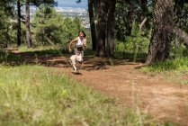 Повне тіло активної жінки-власника, що бігає по сільській дорозі з вірним собакою під час тренувань у гаю в літній день — стокове фото
