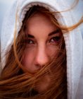 Retrato de mulher enigmática encantadora com cabelo de gengibre voador e no capuz olhando para a câmera no dia ventoso na Galiza — Fotografia de Stock
