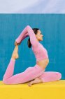 Side view of full body flexible female wearing light pink rash guard and tights in Eka Pada Rajakapotasana on two color background — Stock Photo