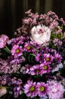 Bouquet von frischen bunten Pfingstrosen und Chrysanthemen in Glasvase auf Holztisch im dunklen Raum platziert — Stockfoto