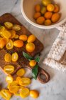 Top view pile of fresh orange cut kumquats on wooden chopping board placed on marble table with towel in kitchen — Stock Photo