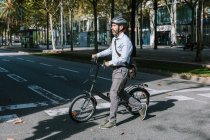 Full length of bearded male worker in helmet crossing asphalt roadway with bicycle on way to work — Stock Photo