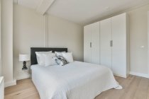 Комфортне ліжко з ковдрою та подушками, розташоване біля вікна в сонячній спальні сучасної квартири — стокове фото