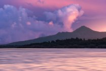 Água do mar fluindo contra a costa com montanha rochosa áspera contra o céu azul colorido com nuvens brancas na natureza ao pôr do sol — Fotografia de Stock