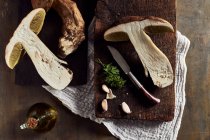 Vista dall'alto dei funghi Boletus edulis tagliati crudi su tagliere di legno con aglio e prezzemolo in cucina leggera durante il processo di cottura — Foto stock