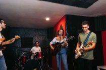 Group of people in casual clothes playing guitars and drums while woman singing and performing song in club — Stock Photo