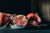 Halved and whole ripe pomegranate on frying pan placed on creased tablecloth on table — Stock Photo