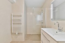 Design criativo do banheiro com toalheiro aquecido contra lavatório com torneira sob espelho em casa de luz — Fotografia de Stock