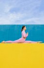Side view of concentrated young woman sitting of Monkey God pose while doing Hanumanasana pose on blue and yellow background — Stock Photo