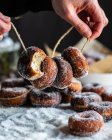 Colheita fêmea irreconhecível segurando saborosos donuts emprestados em pó de açúcar na linha na mesa — Fotografia de Stock