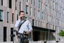 Männlicher Arbeiter in offizieller Kleidung steht mit Fahrrad in der Innenstadt und unterhält sich per Handy — Stockfoto