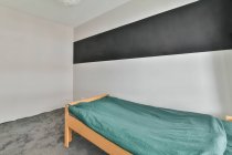 Diseño interior de dormitorio con pared clara y suelo gris y cama individual cubierta con manta turquesa - foto de stock