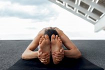 Mulher descalça flexível irreconhecível praticando postura Paschimottanasana no mar durante o treinamento de ioga perto do painel solar na rua na cidade de Barcelona — Fotografia de Stock
