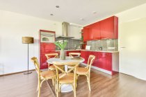 Interior moderno da cozinha com armários vermelhos e mesa de jantar branca decorada com flores em vaso no apartamento contemporâneo — Fotografia de Stock
