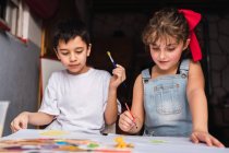 Positive Kinder mit Pinseln malen mit bunten Aquarellen auf Papier am Tisch — Stockfoto