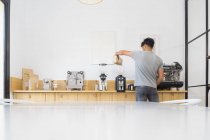 Back view of anonymous male barista pouring coffee beans from bag into modern professional coffee grinder at wooden counter in coffee house — Stock Photo