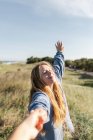 Donna felice in abiti casual tenendo per mano il raccolto partner irriconoscibile mentre in piedi con gli occhi chiusi sul campo erboso — Foto stock