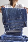 Ritaglio femminile irriconoscibile in camicia bianca accatastamento jeans blu in pile di vestiti dopo il lavaggio — Foto stock