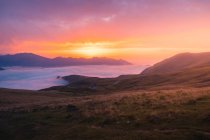 Grassy hill near thick white mist against mountain ridge against colorful sunset sky in wild nature of Spain in Pyrenees — Stock Photo