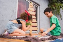 Vista laterale corpo completo di simpatici bambini pittura con vernici colorate e albero di Natale decorativo durante la preparazione delle vacanze in camera — Foto stock