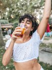 Positivo étnico feminino beber refrescante coquetel e dança enquanto desfruta de festa no jardim de verão — Fotografia de Stock