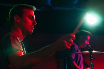 Серьезные молодые парни исполняют музыку на барабанах в клубе с неоновыми огнями — стоковое фото