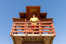 Dal basso bagnino maschio che controlla la sicurezza in mare dalla torre di salvataggio in legno — Foto stock