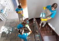 From above of professional female and male housekeepers in uniforms and rubber gloves standing on wooden staircase while cleaning modern spacious house — Stock Photo