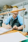 Уважний старший чоловічий майстер в фартусі та окулярах зав'язує стрічки на дерев'яній дошці перед роботою над друкарським верстатом — стокове фото