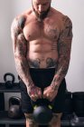 Powerful shirtless bodybuilder with tattoos doing exercise with heavy kettlebell during functional training in gym — Stock Photo