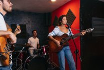 Grupo de pessoas em roupas casuais tocando guitarras e bateria enquanto a mulher cantando e cantando música no clube — Fotografia de Stock