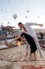 Corps entier de couple pieds nus dansant ensemble sur le toit-terrasse contre les montgolfières volant dans un ciel sans nuages — Photo de stock