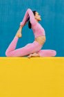 Side view of full body flexible female wearing light pink rash guard and tights in Eka Pada Rajakapotasana on two color background — Stock Photo