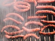 From above various types of tasty sausages roasting on grill grate above charcoal in countryside during barbecue in countryside on summer day — Stock Photo